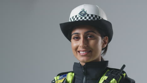 Studio-Portrait-Of-Smiling-Young-Female-Police-Officer-Against-Plain-Background