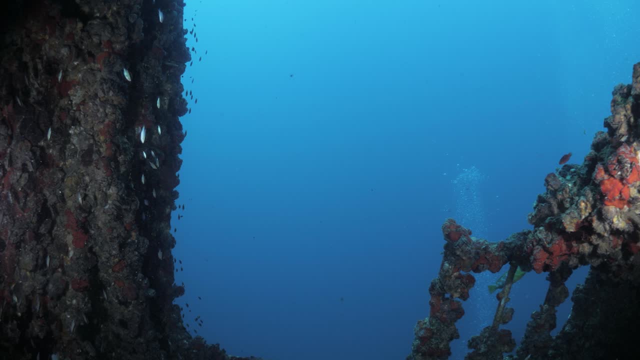 Unique scuba divers view swimming through the recently scuttled Navy boat the Ex-HMAS Tobruk artificial reef showing the sunlight penetrating through the side of the sunken ship