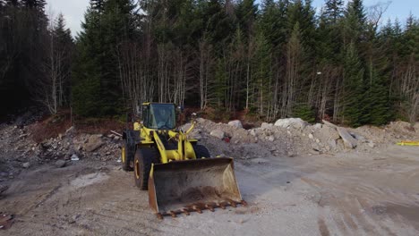 dando vueltas alrededor de la excavadora en un sitio de construcción con bosque en el fondo
