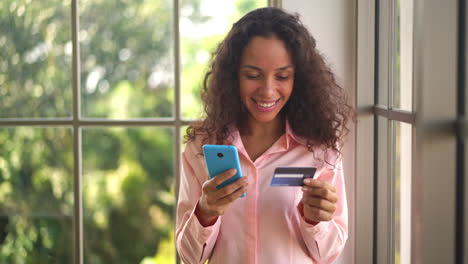 beautiful latin woman using smartphone with hand holding credit card