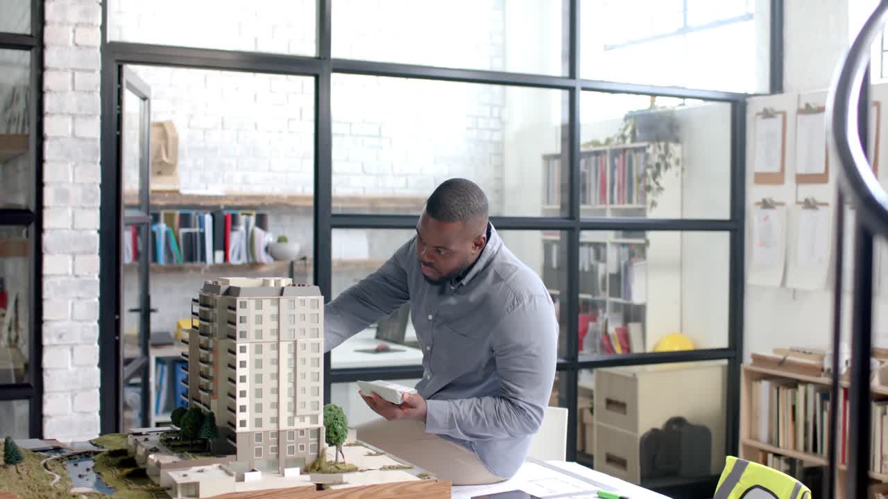 concentrado afroamericano hombre de negocios casual inspeccionando la ciudad modelo en la oficina en cámara lenta