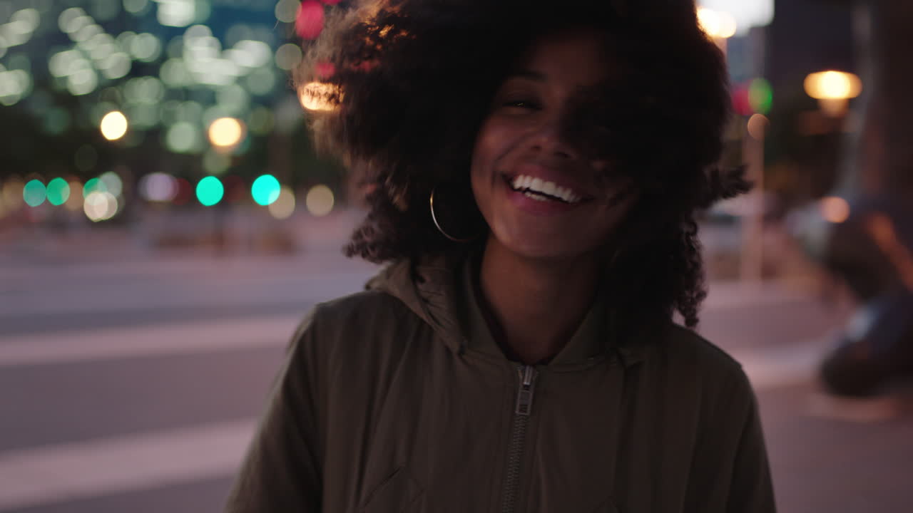 ritratto di elegante giovane donna afroamericana con afro che ride giocosa che gode della vita notturna in città il vento che soffia i capelli stile di vita urbano