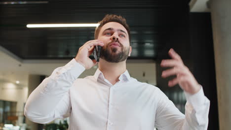 un joven empresario caucásico sonriente hablando por teléfono inteligente discutiendo el trabajo en el vestíbulo de la oficina del hotel
