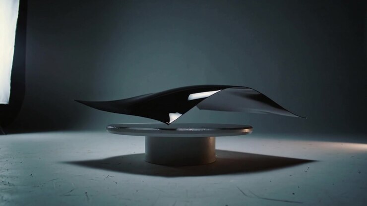 Oscillating thin sheet forming wavy curves while floating above pedestal in studio