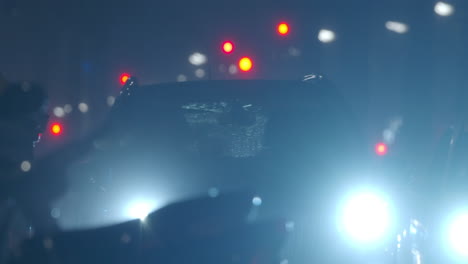 Car-with-dazzle-lights-moving-slowly-in-night-city-under-the-rain