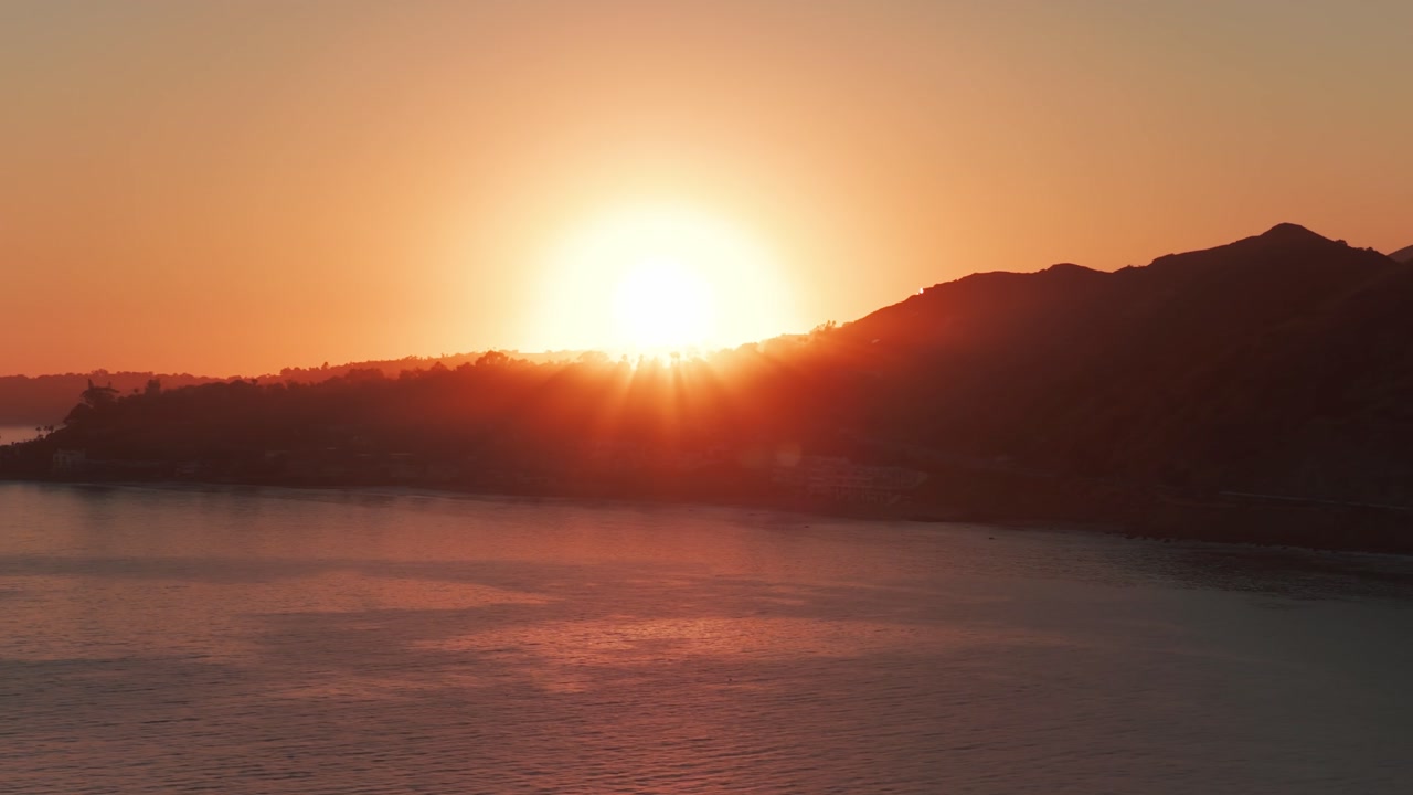 Telephoto dolly aerial shot of the sun setting over Point Dume in Malibu, California. 4K