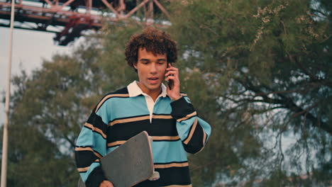 Positive-hipster-calling-cellphone-city-closeup.-Man-walking-skateboard-vertical