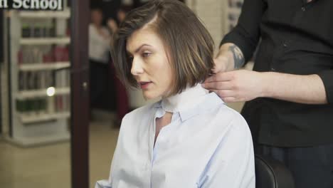 Beautiful-woman-with-short-brown-hair-sitting-in-a-chair-in-a-hair-salon-while-a-hairdresser-putting-on-white-protective-collar