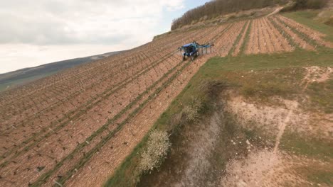 an fpv drone's view while orbiting downwards towards a tractor sprayer fertilizing the vineyards in chablis, france