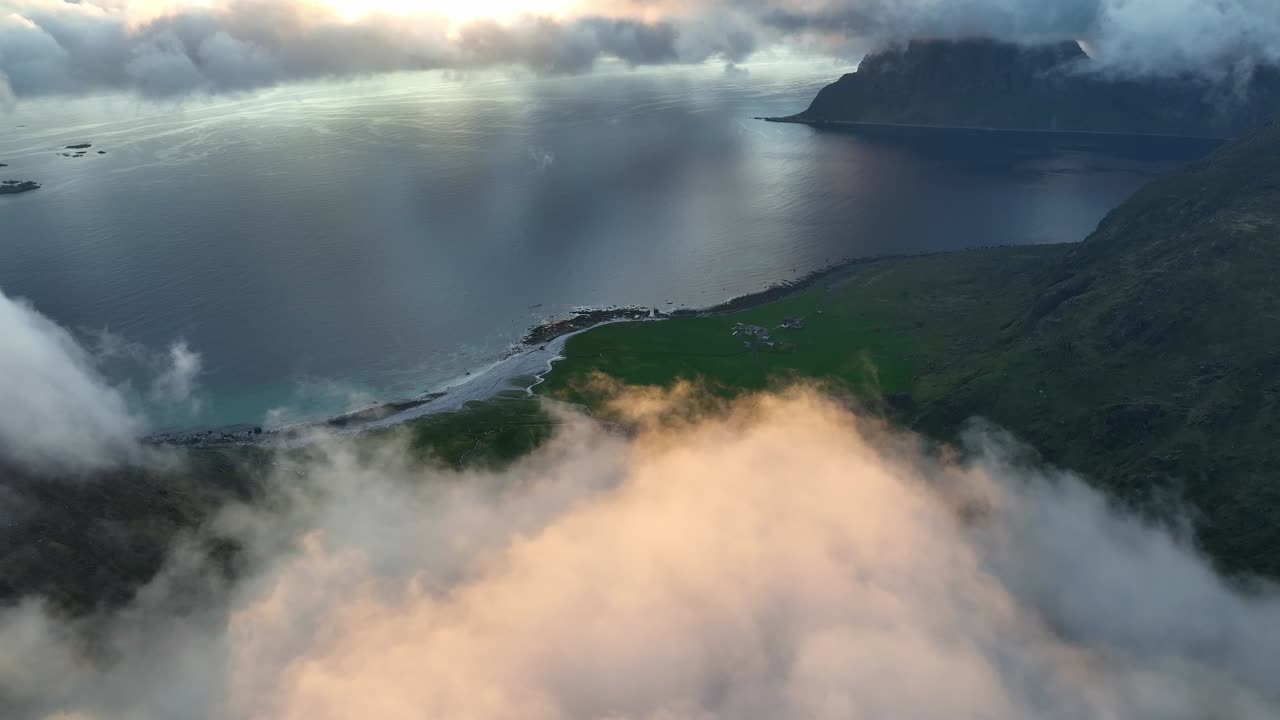 Midnight light colors clouds pink above Utakleiv beach and ocean in Lofoten. Fog wraps nearby peaks