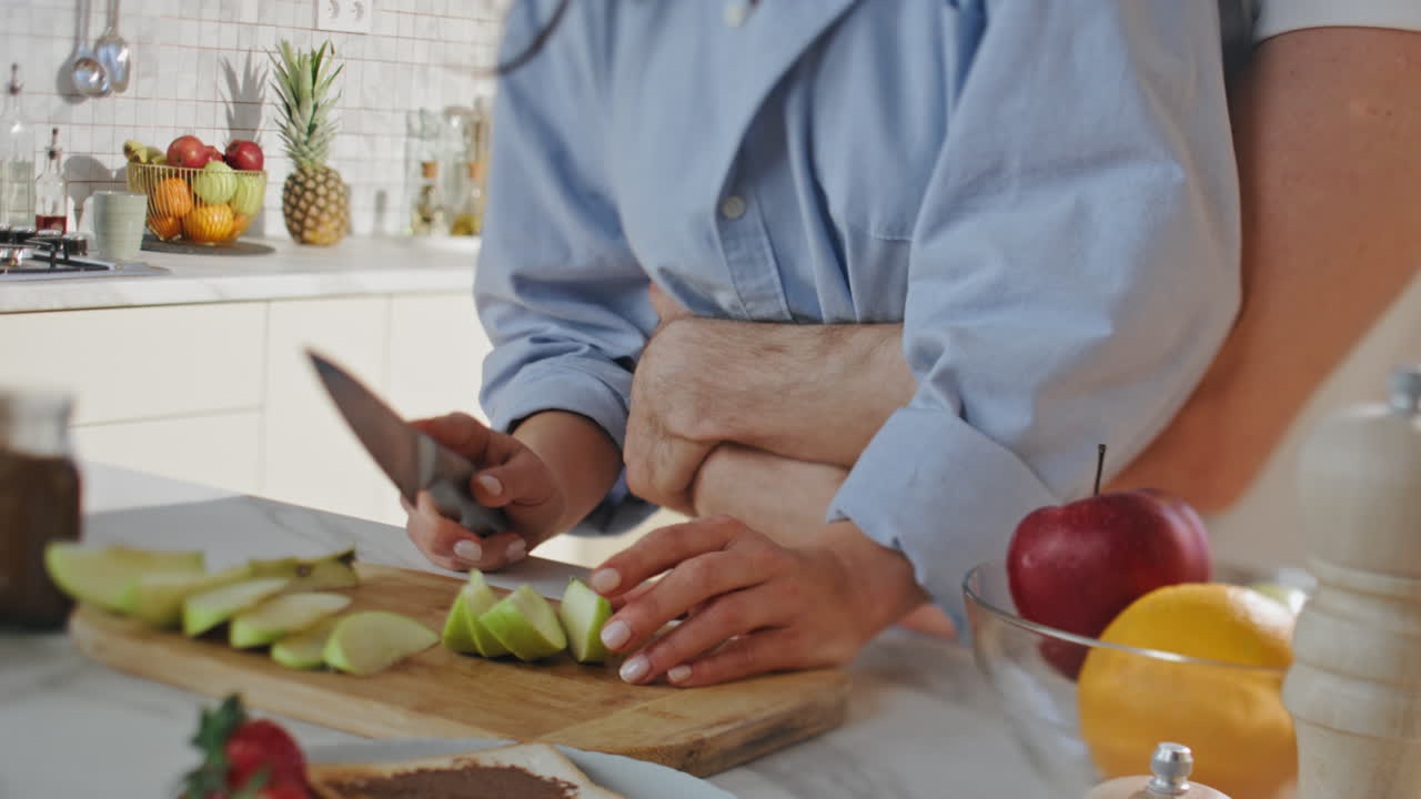 pareja irreconocible preparando comida en la cocina de cerca. manos cortando manzana
