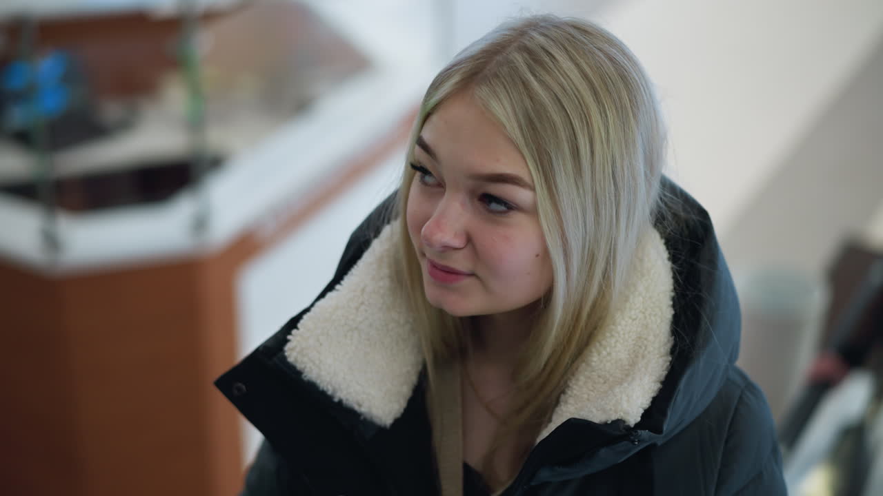 улыбающаяся женщина поднимается на движущемся эскалаторе торгового центра, с размытым городским фоном с современными торговыми структурами и элементами современного дизайна