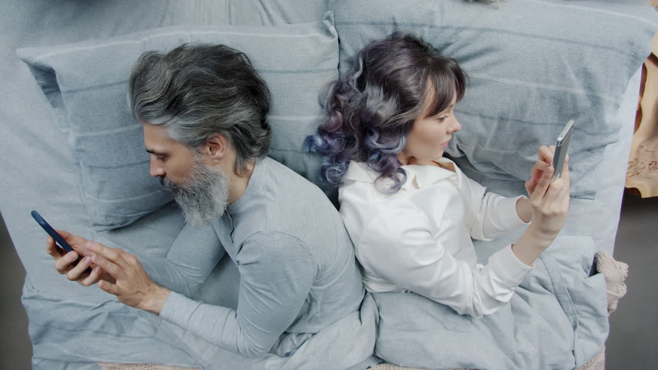 Couple Lying in Bed, Back to Back, Using Phones