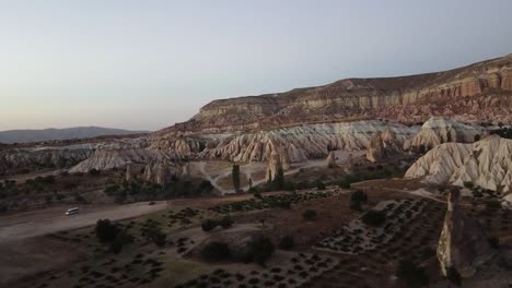 Aereal-view-of-a-group-of-cars-exploring-the-red-valley-of-Cappadocia,-Turkey,-at-sunset