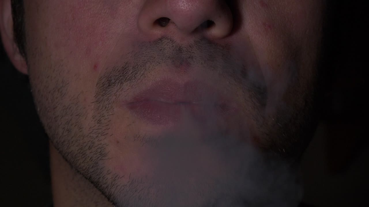 крупным планом рот молодого взрослого мужчины с щетиной, курящего и затягивающегося сигаретой