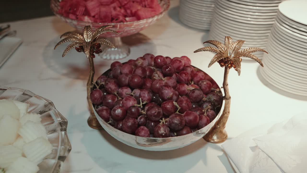 bowl of red grapes with golden palm handles on marble buffet setup