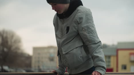 close-up of a young boy working out on an iron bar, wearing a gray sweater and beanie, the background features a blurred view of people and buildings
