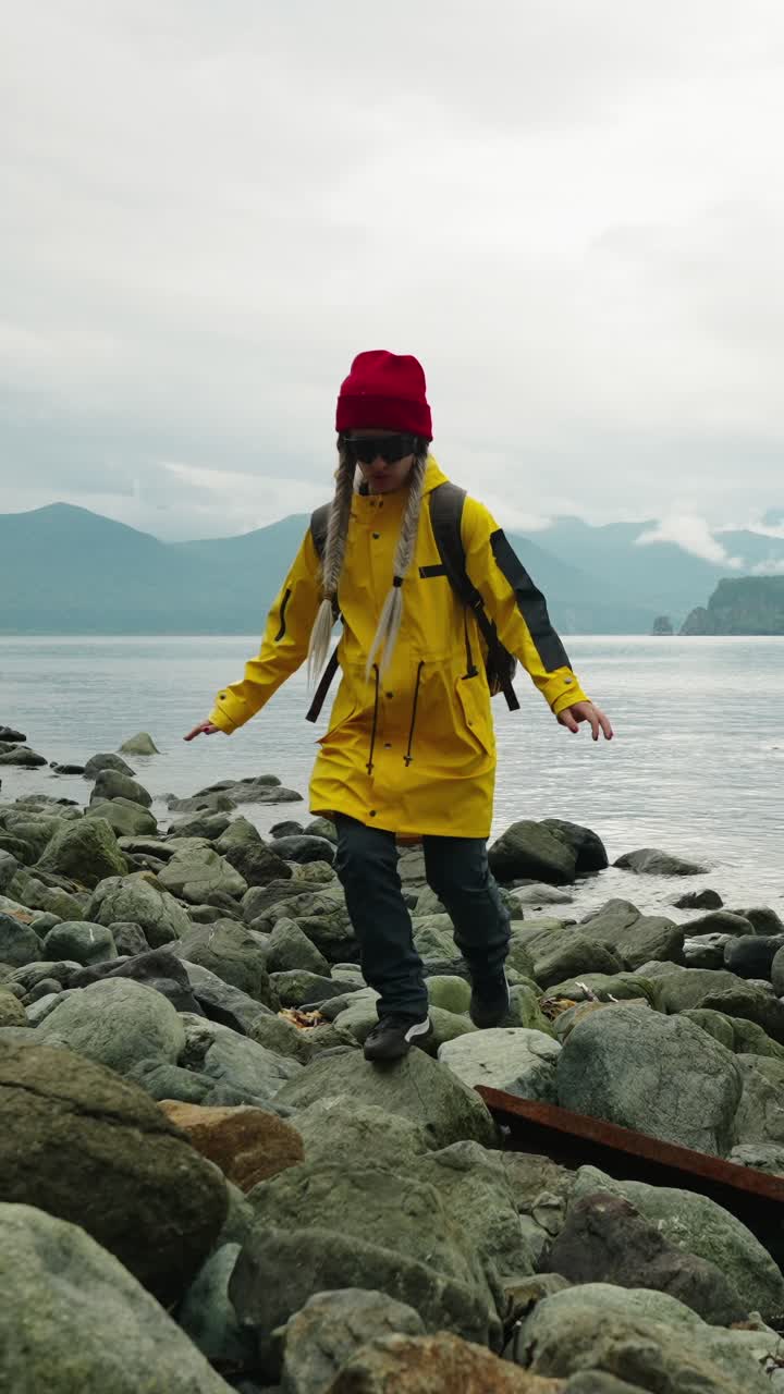Woman in Yellow Raincoat Walking on Rocky Beach