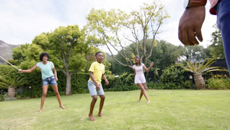 Felices-Padres-Afroamericanos,-Hijo-E-Hija-Saltando-En-Un-Jardín-Soleado,-Cámara-Lenta