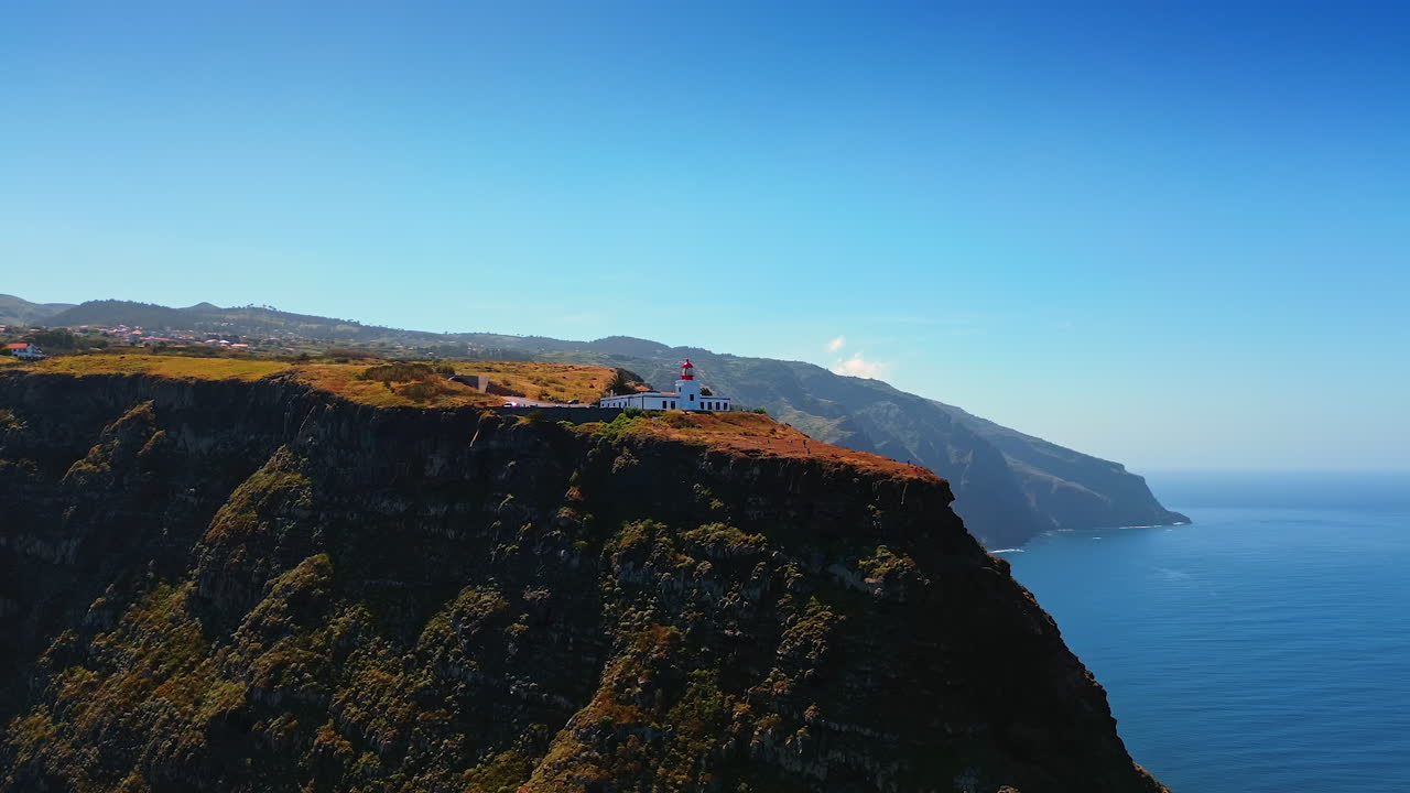 Huge mountains with steep cliffs with a beautiful lighthouse on top. Scenery of the shore of the Madeira Islands, Portugal. Aerial view.