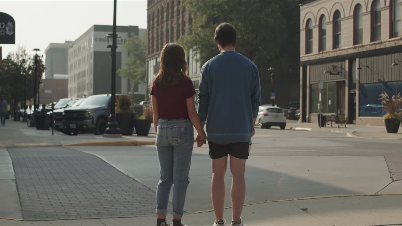 Young couple holding hands standing downtown looking at the cars and buildings with camera in hand.