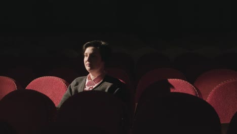 woman sitting in comfortable red chairs in dark theater