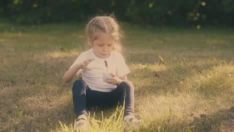 small girl looks at yogurt container with spoon and eats