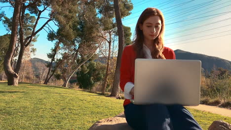 Una-Mujer-Feliz,-Atractiva,-Joven-Y-Caucásica-En-El-Parque,-Escribiendo-En-Su-Computadora-Portátil