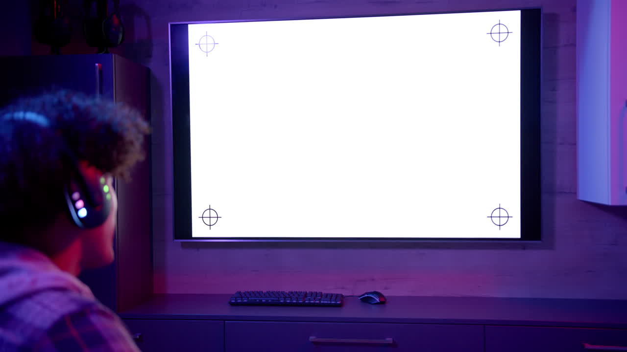 Watching large screen, man with headphones sitting at desk with keyboard and mouse