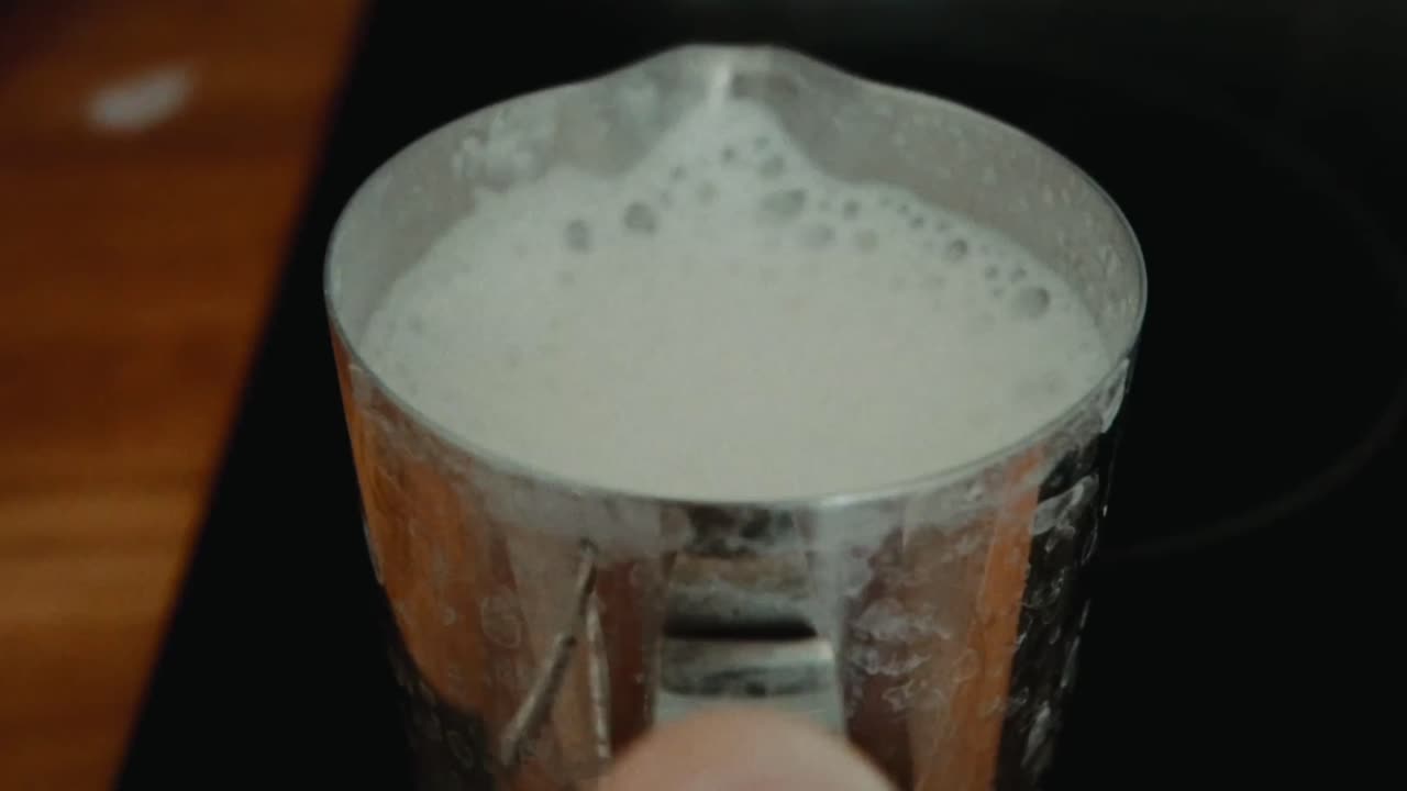 punto de vista fijo, la leche se vierte con gracia de la tapa en una taza de café, simbolizando la comodidad y el encanto ritual de las rutinas matutinas y los placeres simples