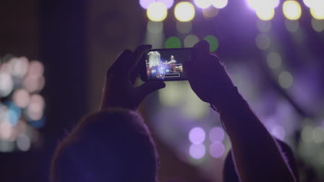 un espectador toma una foto panorámica del escenario con reflectores a través de un teléfono inteligente en un concierto de música al aire libre