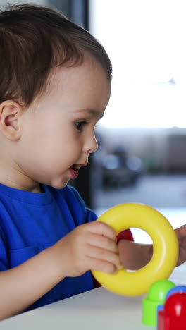 charming cute caucasian baby boy sits at the desk playing with pyramid. toddler puts on the colorful rings on hands and clapping hands cheerfully. vertical video