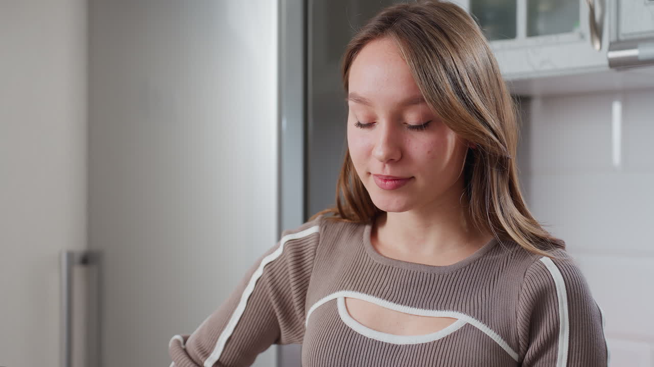 갈색 옷을 입은 우아한 여성은 따뜻한 미소로 우아하게 포즈를 취하고, 현대적인 부에서 내려다보고, 그녀의 자신감 넘치는 표정과 편안한 자세