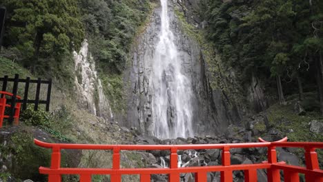scenic view of nachi falls plunging down a steep cliff face, framed by lush greenery and a traditional red bridge in nachikatsuura, japan