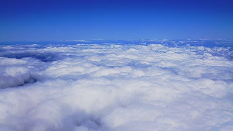 Eine-Atemberaubende-Luftaufnahme-Aus-Einem-Flugzeug,-Das-Tagsüber-über-Flauschige-Weiße-Wolken-Inmitten-Des-Strahlend-Blauen-Himmels-Gleitet