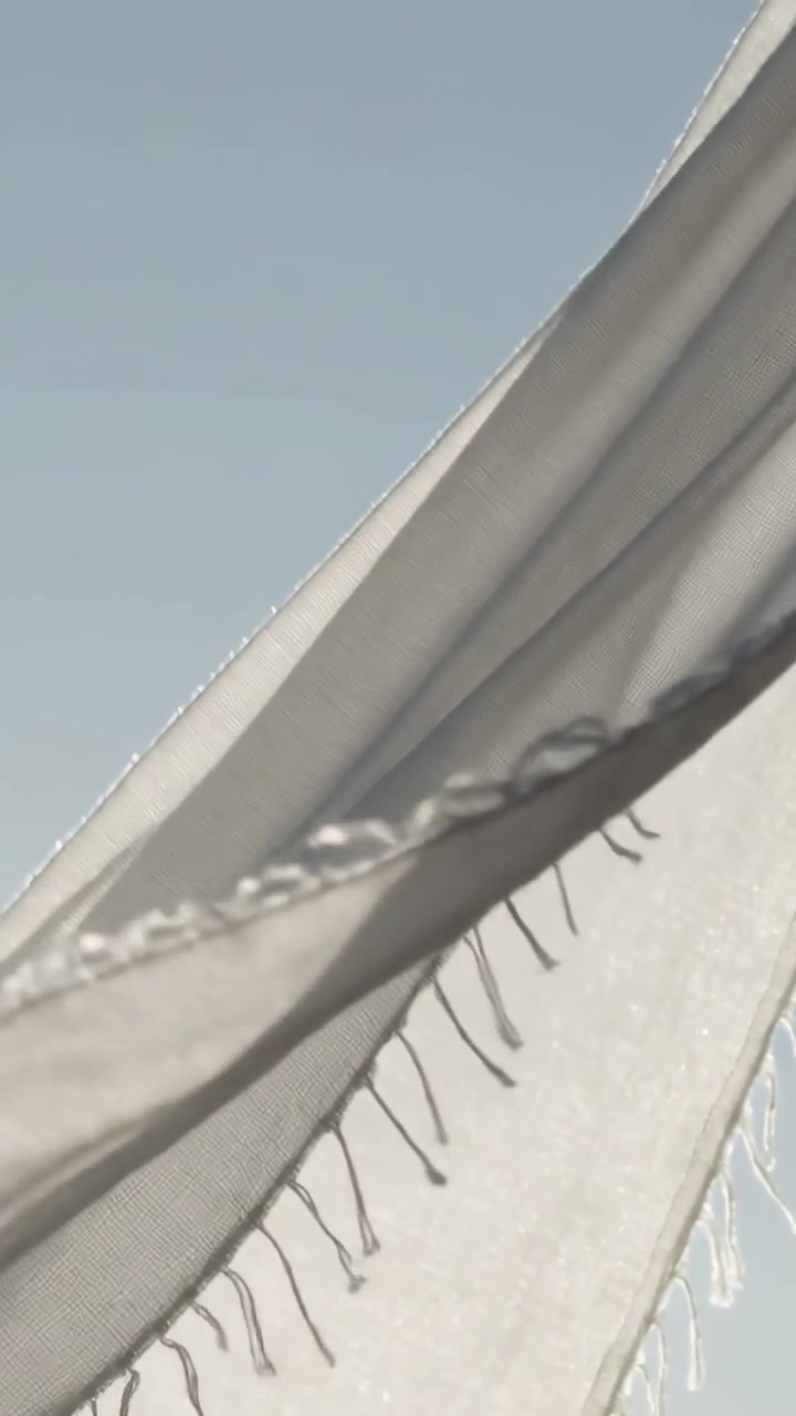 Vertical video: Billowing fabric revealing darker lining against pale sky in breeze, frayed edge