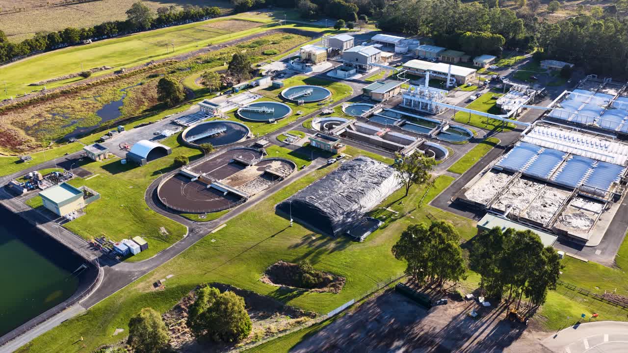 Drone footage pans across a large wastewater treatment plant in Gold Coast, Australia, showing water tanks, green spaces, and facility infrastructure in bright daylight