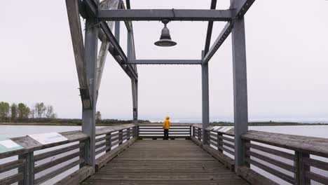 Totale-Aufnahme-Einer-Person-In-Einer-Gelben-Jacke,-Die-Am-Hafen-Steht-Und-Einen-Pier-Mit-Fischerbooten-überblickt