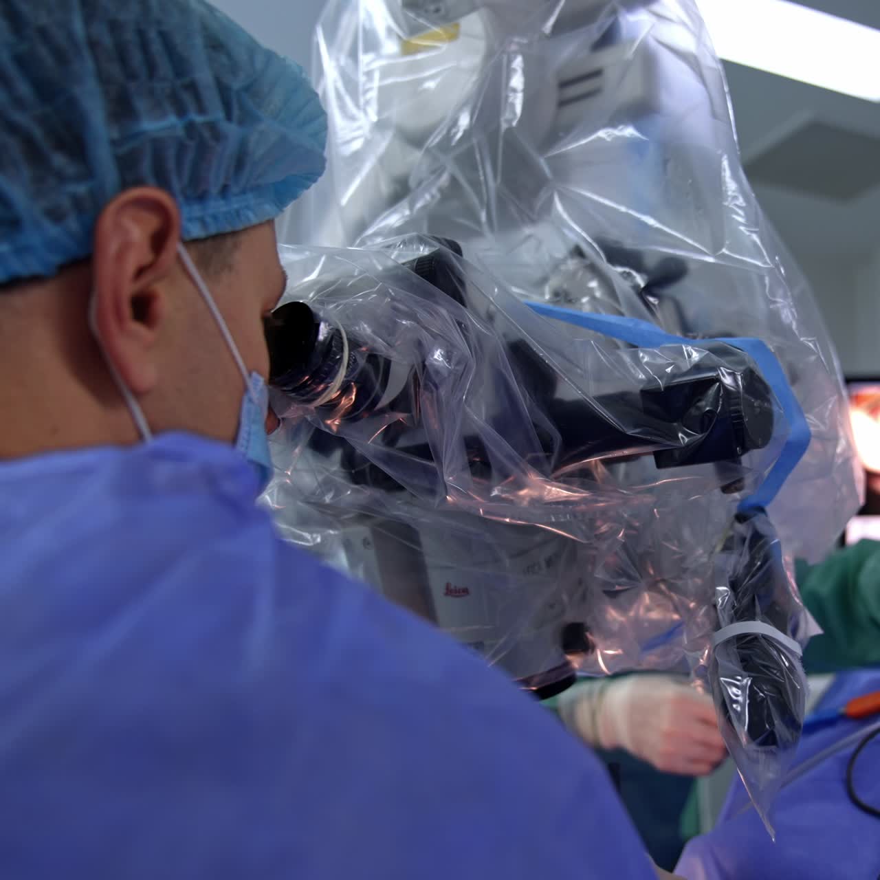 Rear view of a medic in mask looking into microscope. Close up. Screen showing the procedure process at backdrop in blur