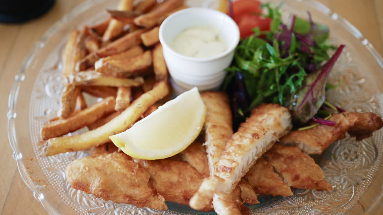 Fish and chips serveras med krispiga pommes frites, fräsch sallad, citronklyfta och krämig dippsås