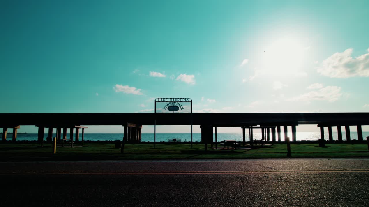Golden hour view of Lake Maurepas Underpass bridge with grassy park and calm lake, perfect road trip scenery.