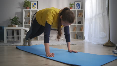 young woman is doing physical exercise at home workout in apartment in weekend tensing muscles of legs and arms sportswoman is keeping fit