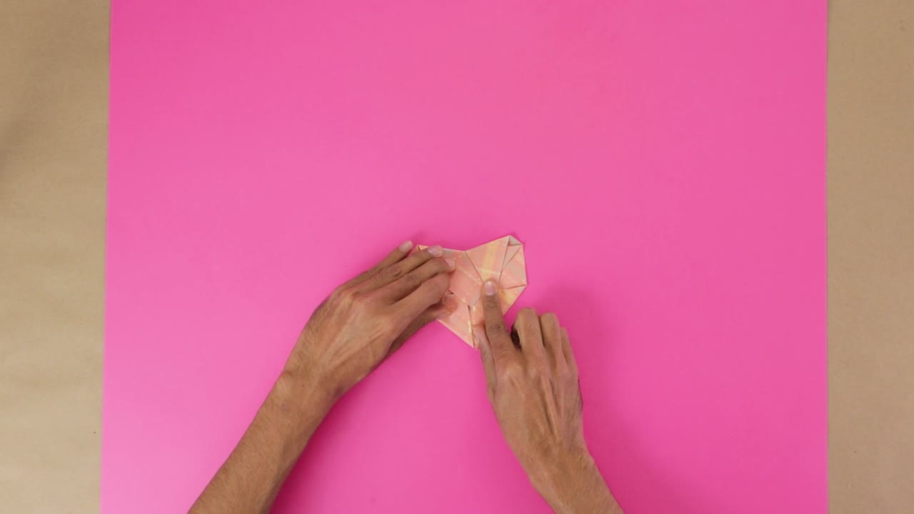 Folding heart from origami paper for Valentines day, pink background