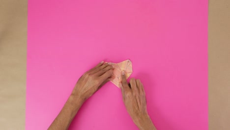 folding heart from origami paper for valentines day, pink background