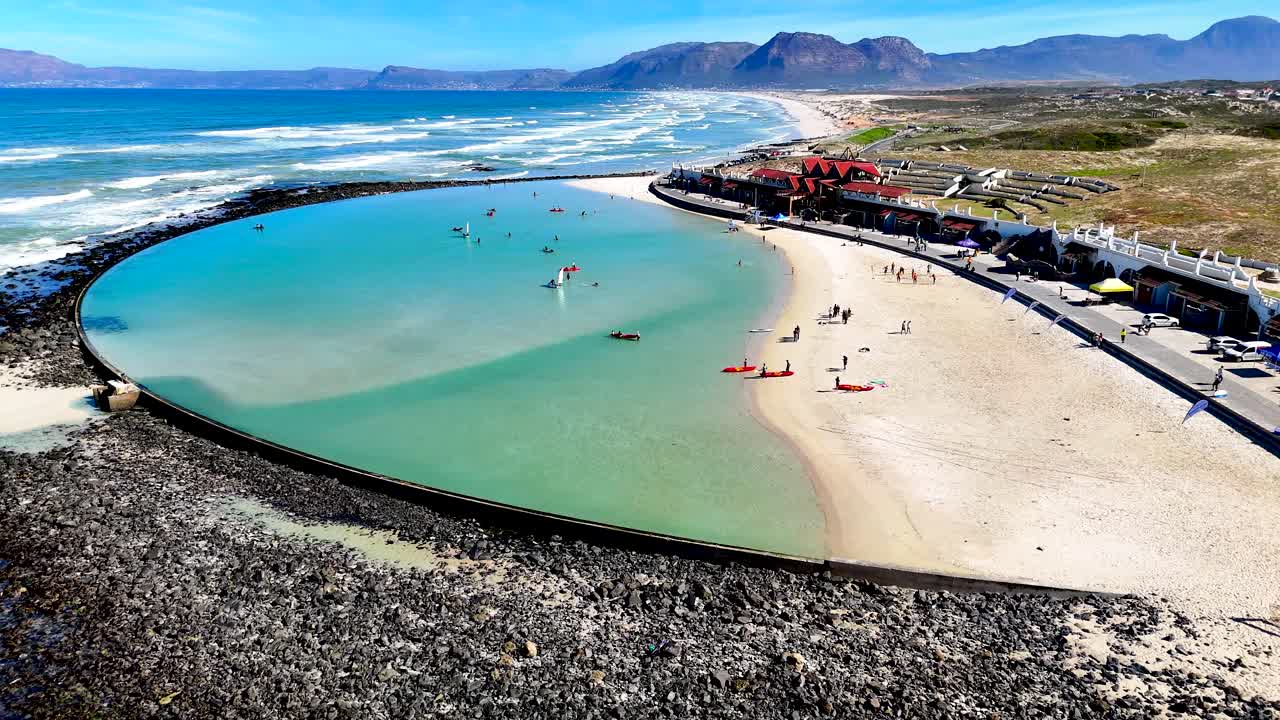 Drone clip of a large tidal pool with a sandy beach and the coastline in the background