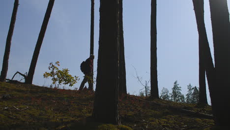 man is travelling alone in forest walking with backpack and fishing rod silhouette of his figure against sky