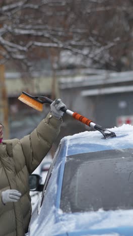 woman removing snow from car in winter