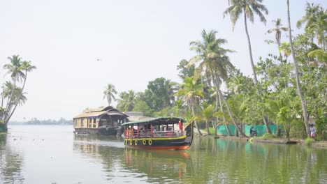 Dos-Barcos-Moviéndose-Hacia-La-Cámara-En-Los-Remansos-De-Kerala,-Uno-Más-Moderno-Y-Más-Pequeño-Y-El-Otro-Más-Grande-Y-Una-Casa-Flotante-Tradicional