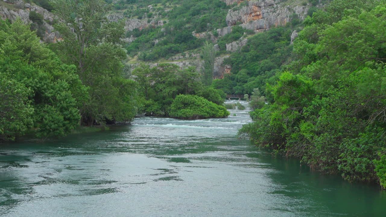 Waterfall in the greenery of Krka National Park with mountains in the background