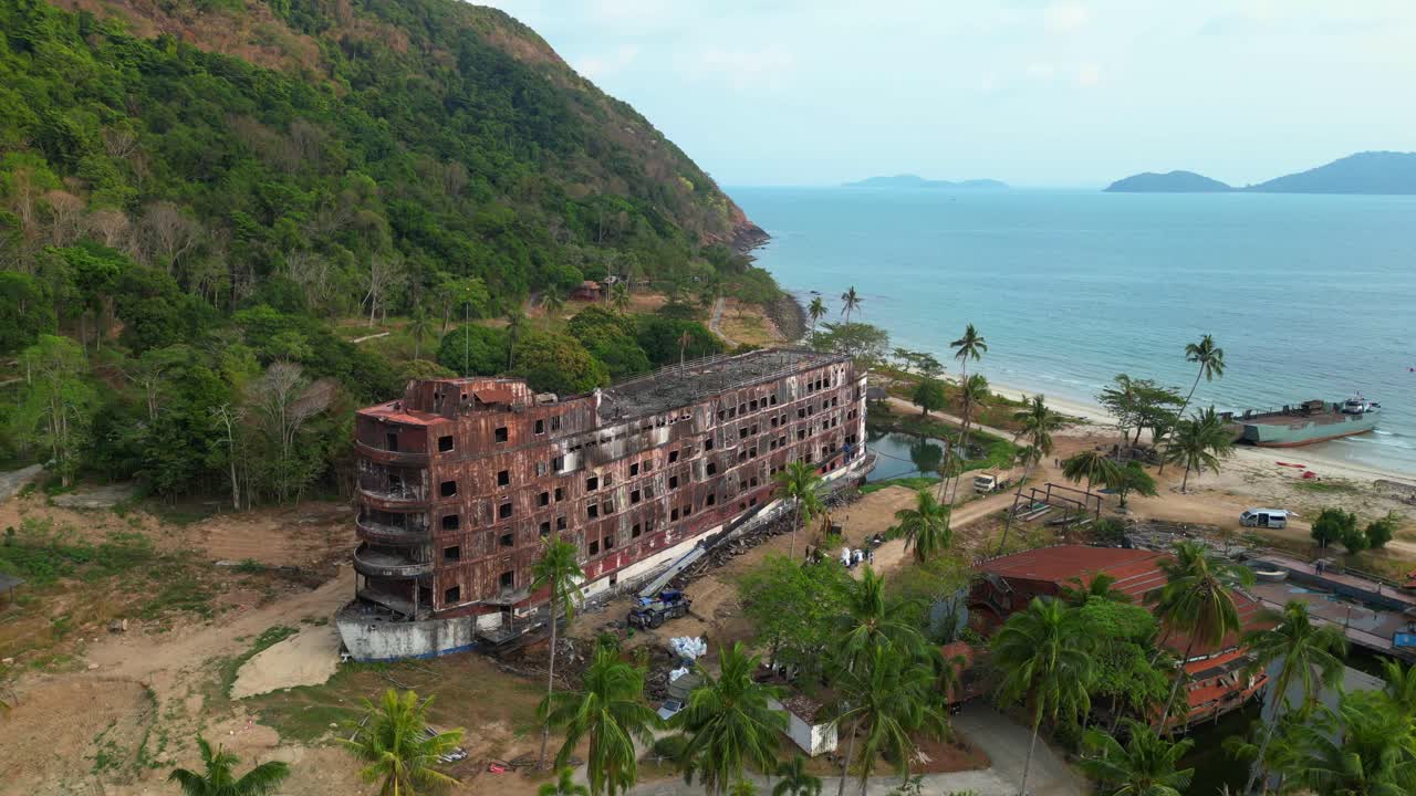abandoned rusty ghost ship on Koh Chang on tropics island bay, Thailand, during sunset, with a crane working on it. Best aerial view flight panorama overview drone